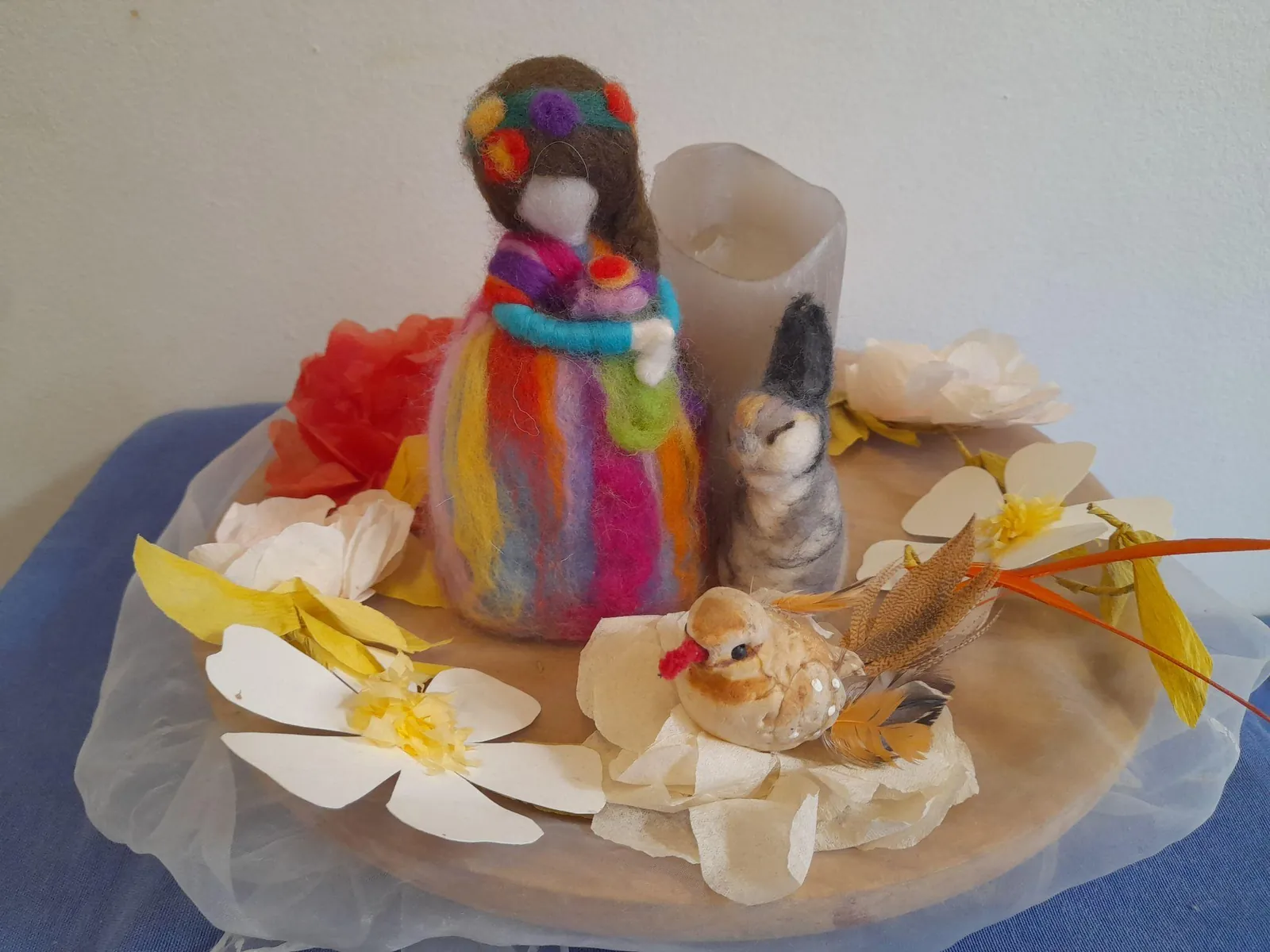 Figura de feltre de colors amb flors de paper i ocells sobre una safata, a la taula de temporada
