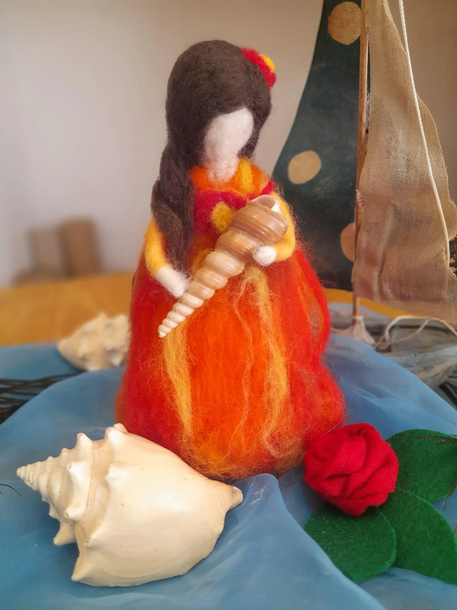 Figura de feltre vermella i taronja que sosté una petxina, envoltada de petxines i una rosa